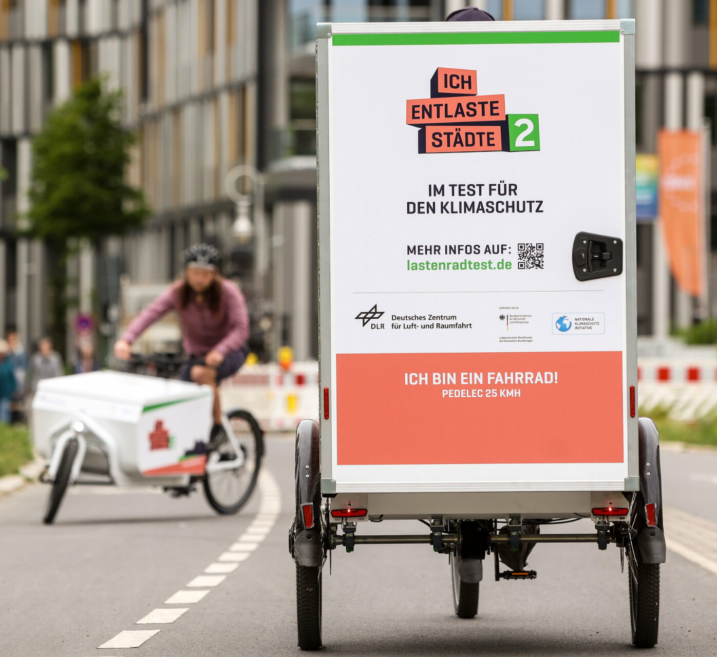 Ein dreirädriges Lastenrad mit Kofferaufbau fährt auf einem Radweg